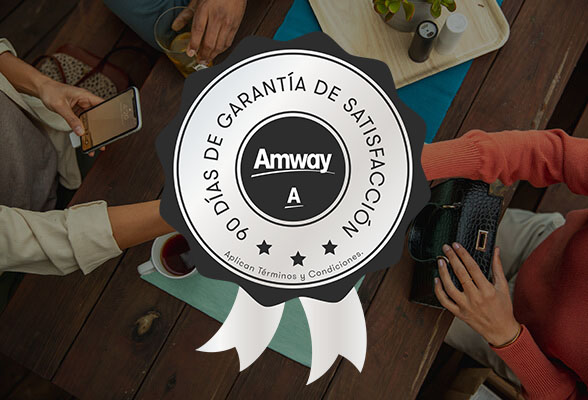 Personas trabajando en una mesa de trabajo con una tableta. Logotipo de la promesa de Amway en el centro. Conoce nuestra garantía de satisfacción Amway.