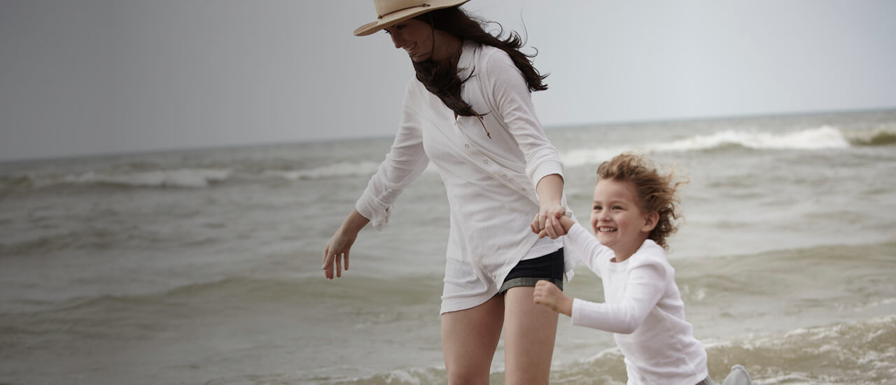 Imagen de una mujer y un niño jugando en la playa. Aprende acerca de los productos Safer Choice de Amway Home.